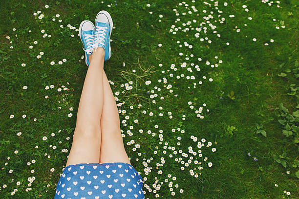 Unrecognizable female sitting on a green grass among daisies, enjoying a carefree summer day at the park.