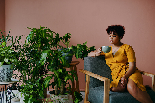 Shot of a young woman drinking coffee while relaxing with plants around her at home