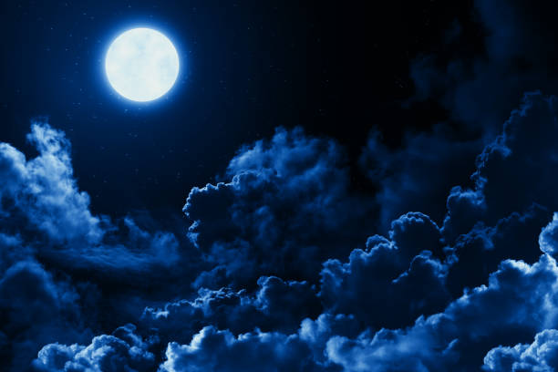 Mystical bright full moon in the midnight sky with stars surrounded by dramatic clouds. Dark natural background with twilight night sky with moon and clouds stock photo