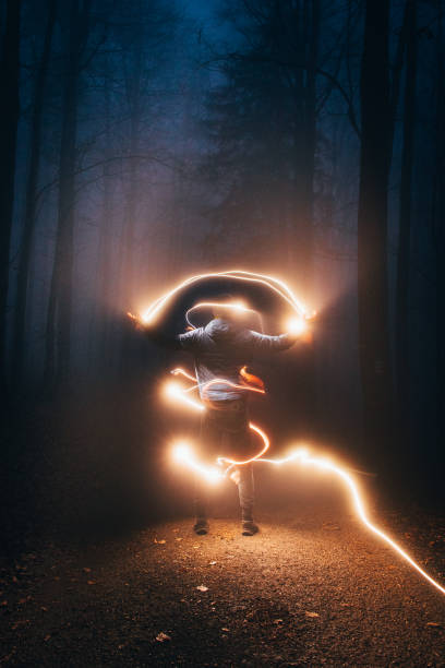 mystique in the autumn forest, where a boy in a blue jacket flies light from his left hand to his right and around his whole body. Mysterious siuleta in the wild surrounded by many lights stock photo