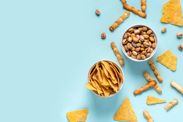 Nachos, pistachios and cheese sticks Beer snack, copy space. Nachos, pistachios and cheese sticks in white bowls on a blue background, top view, flat lay, free space for text. Minimal style. snack stock pictures, royalty-free photos & images