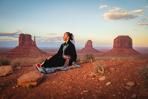 A Native American woman dressed in traditional Navajo clothing, poses in the landscape of Monument Valley, on the border of Utah and Arizona.
