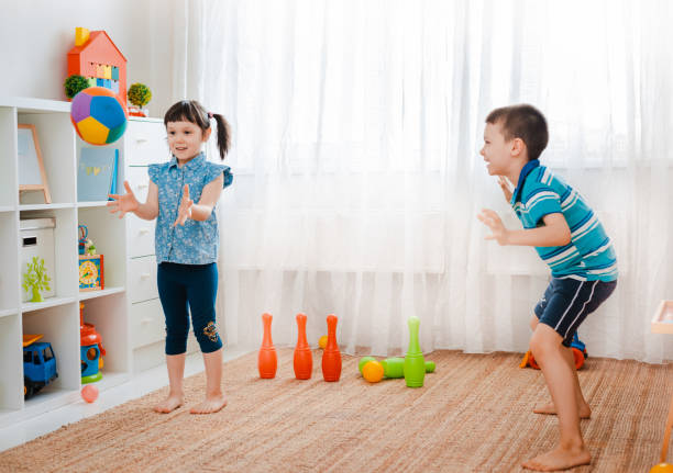 native children a boy and a girl play in a children's game room, throwing a ball. The concept of interaction of todlers, communication, mutual play, quarantine, self-isolation at home stock photo