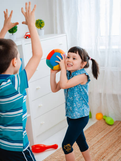 native children a boy and a girl play in a children's game room, throwing a ball. The concept of interaction of todlers, communication, mutual play, quarantine, self-isolation at home stock photo