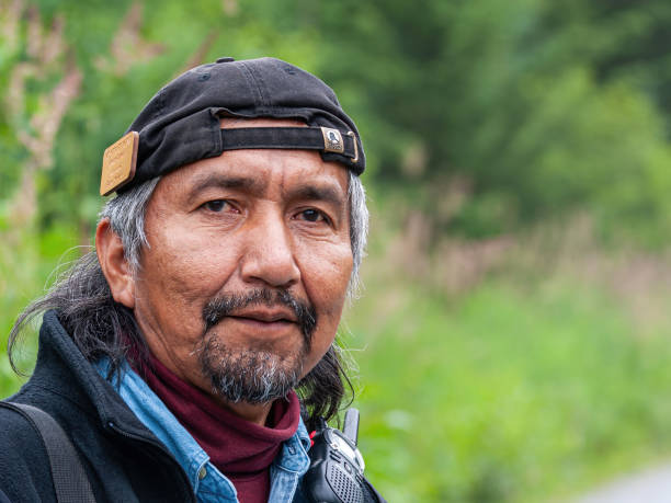 Native Tlingit man facial closeup,  Hoonah, Alaska, USA Hoonah, Alaska, USA - July 18, 2011: Facial closeup of native Tlingit man with reversed black cap on bearded head working as a forest guardian. Faded green as background. alaska native stock pictures, royalty-free photos & images