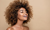 Gladness on the face of perfectly looking brown skinned young woman.. Natural, dense afro hair on the head of young beautiful model, white toothy smile on her face. Girl with vibrant, melanin-rich skin tone.