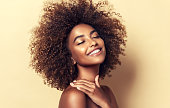 Portrait of perfectly looking brown haired young woman. Natural, dense afro hair on the head of young beautiful model, white toothy smile on her face. Girl with vibrant, melanin-rich skin tone. Closed eyes and happy smile.