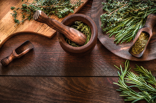 High angle view of natural aromatic herbs like dill, thyme, oregano and rosemary on wooden mortar and over dark brown wooden table. Predominant colors are brown and green. copy space on the lower part of the image. Low key DSLR photo taken with Canon EOS 6D Mark II and Canon EF 24-105 mm f/4L