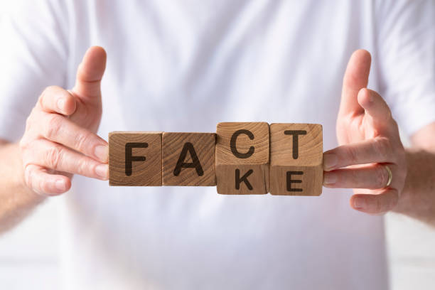 Natural teak wood blocks with the words 'Fact and Fake' written on two angled sides of them, being held up by a man. stock photo