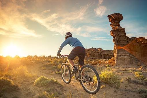 a man pedals his mountain bike while cycling in solitude.  the sunshine creates a lens flare in the desert landscape.  horizontal wide angle composition with copy space.   gallup, new mexico.