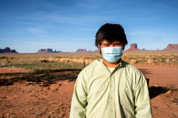 A Navajo Teenage Boy Living In Monument Valley Poses With A Mask For Protection From The Coronavirus A teenage Navajo boy wears a mask for protection from Covid19 as he stands with Monument Valley in the background navajo nation covid stock pictures, royalty-free photos & images