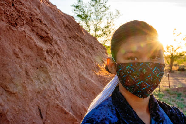 A Navajo Teenage Girl Wearing A Mask Stands By Her Family Hogan As The Sun Is Setting A teenage Navajo girl wears a mask for protection from Covid19 as she stands by a hogan at sunset navajo nation covid stock pictures, royalty-free photos & images