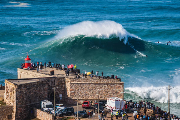 nazare, portogallo, surfista che cavalca un'enorme onda vicino al forte del faro di nazare - nazaré foto e immagini stock