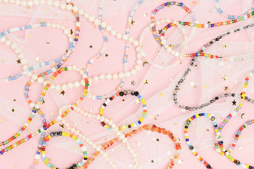 Necklaces and bracelets made from colorful beads and pearls on a pink background.