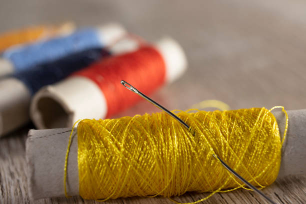 a needle in threads on a light wooden background. colored textile threads for sewing on the table. - linha artigo de costura imagens e fotografias de stock