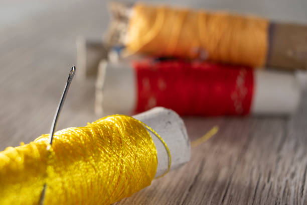 a needle in yellow threads on a light wooden background. colored textile threads on the table. - linha artigo de costura imagens e fotografias de stock