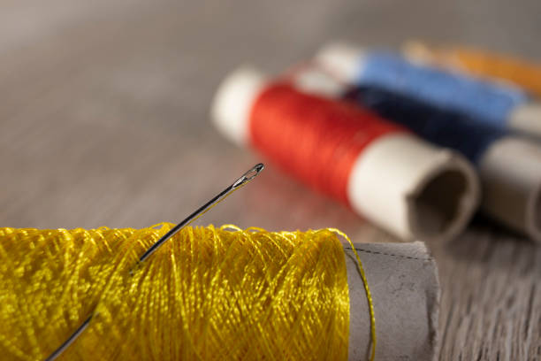 a needle in yellow threads on a light wooden background. - linha artigo de costura imagens e fotografias de stock