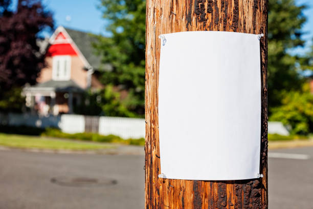 Neighborhood Post Photo of a blank sheet of white paper fastened to a wooden electrical pole, neighborhood houses visible in the background. pole stock pictures, royalty-free photos & images