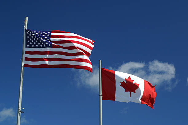 US and Canadian flags wave in wind on graduated blue background with clouds. We have numerous American and Canadian flag images in our portfolio.