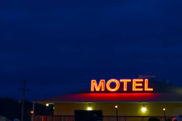 A neon sign reading MOTEL,  glows at dusk with a clear, blue sky in the background. stock photo