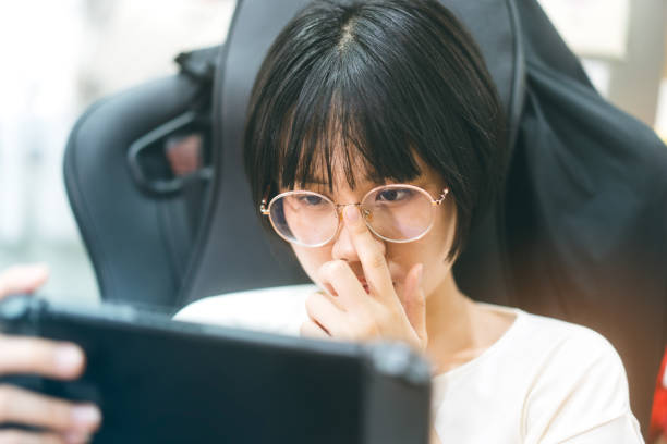 Nerd style young adult asian gamer woman wear eyeglasses play a handheld online game. stock photo