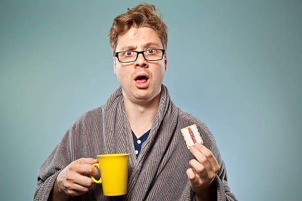 Nerdy guy drinking coffee and eating a biscuit stock photo