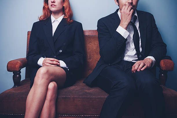 A nervous businessman sitting next to confident woman Nervous businessman is biting his nails while sitting next to a confident businesswoman as they are both waiting to be interviewed for the same job interview nerves stock pictures, royalty-free photos & images