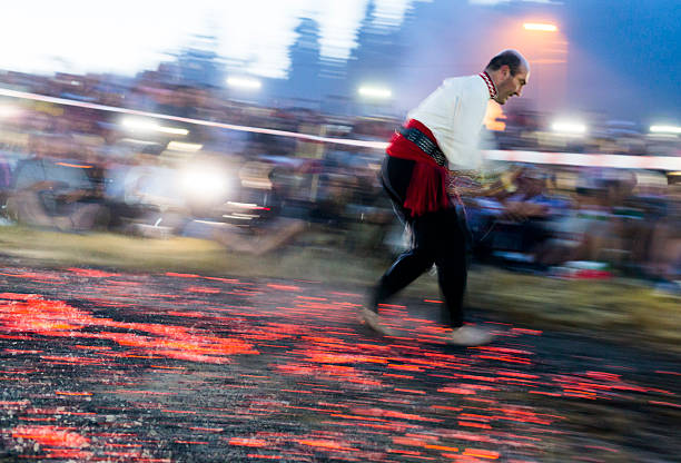 Nestinar walking on fire Rozhen, Bulgaria - July 18, 2015: A man is walking on fire during a  religious show called "nestinarstvo" performed as part of the programat of The National Folk Festival of Rozhen. The fire ritual involves a barefoot dance on smouldering embers performed by "nestinari". It is usually performed on the square of the village in front of the whole population on the day of Sts. Constantine and Helen. firewalking stock pictures, royalty-free photos & images