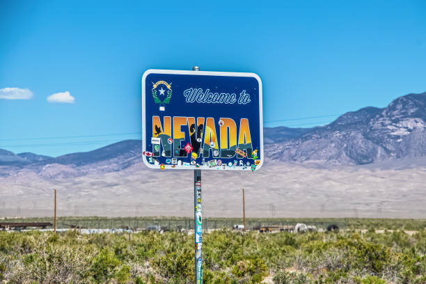 Nevada border USA - Welcome to Nevada sign with stickers partly covering it with wire fence and desolate purple mountains blurred in background stock photo