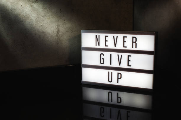 Never give up motivational message on a light box Never give up motivational message on a light box in a cinematic moody background adversity stock pictures, royalty-free photos & images