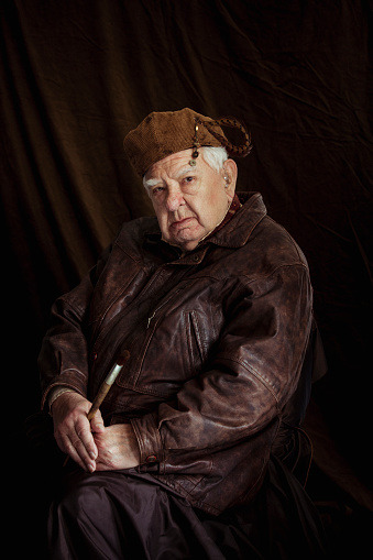 Rembrandt inspired portrait. A mature man is sitting against a studio background dressed in a 19th Centruty style looking at the camera while holding a paintbrush.