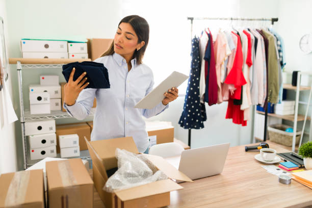 New clothes and products to update the online shop Female entrepreneur working on her business start-up and unpacking boxes from her suppliers for the online clothing shop textile industry photos stock pictures, royalty-free photos & images