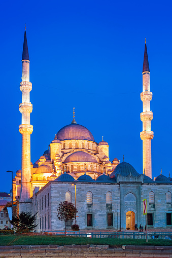Stock photograph of the landmark New Mosque (Yeni Cami Mosque) on Eminonu Square in Istanbul Turkey illuminated at twilight blue hour.