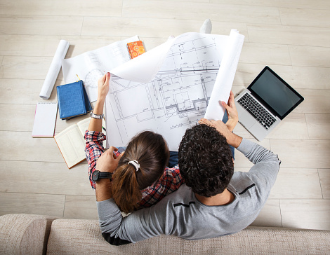 Young couple sitting on the floor and looking at the blueprint of new home.