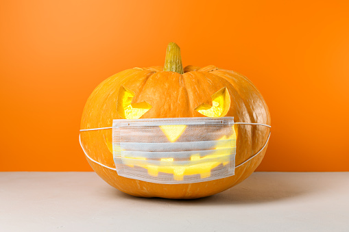 New normal concept. Glowing Halloween pumpkin in a protective medical mask on a orange background. Copy space.