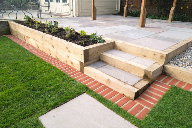 New steps in a garden or back yard leading to a raised patio, alongside a new raised flowerbed made using wooden sleepers. A mowing strip of bricks is in front of newly laid turf. stock photo