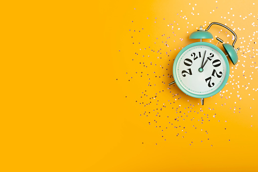 New Year 2022 banner background concept. 2021 changes to 2022 on an alarm clock on a yellow background with festive glitter on New Year's Eve and Christmas. High quality photo