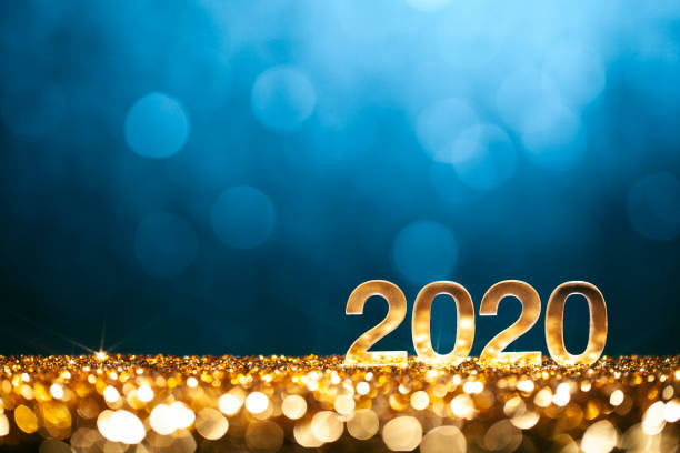 Golden numbers 2020 and Christmas decorations on glitter and defocused lights.