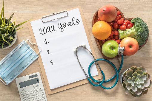 2022 New Year Goals in new normal lifestyle, work-life balance with face mask safety awareness from covid-19, healthy food, good heart health, blank resolution list on white paper medical clipboard