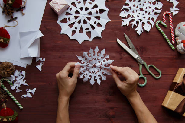 New Year's, Christmas concept. Female hands cut snowflakes from paper. In the background lie gifts, Christmas decorations on a wooden background. stock photo