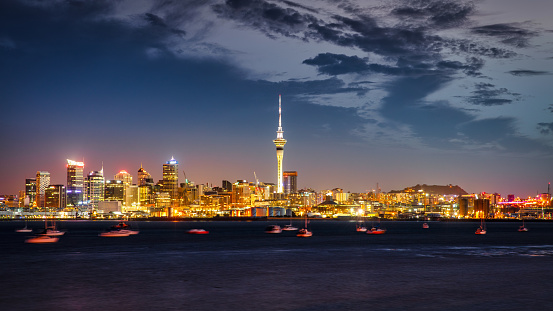 New Zealand Auckland Skyline - Cityscape Panorama. Iconic illuminated Sky Tower of Auckland and cityscape of downtown Auckland in sunset twilight - night. Yachts, tourboats and motorboats anchored in the Auckland harbour bay.  Auckland, New Zealand, Oceania