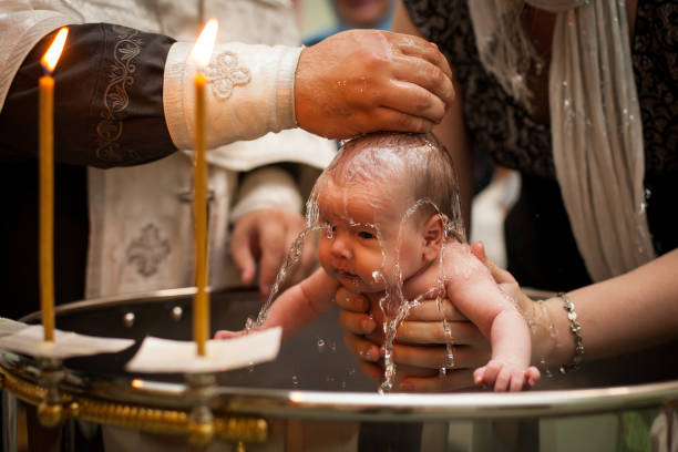 聖なる水の中で生まれたばかりの赤ちゃんのバプテスマ。母親の手を握っている赤ちゃん。幼児は水に入る。フォントのバプテスマ - カトリック ストックフォトと画像
