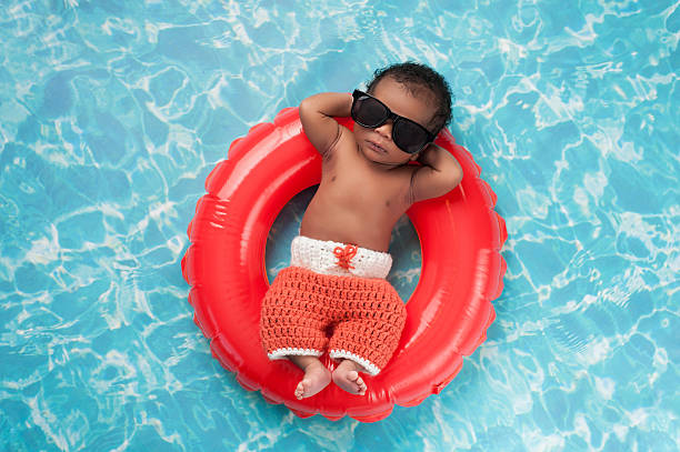 Newborn Baby Boy Floating on a Swim Ring Two week old newborn baby boy sleeping on a tiny inflatable swim ring. He is wearing crocheted board shorts and black sunglasses. babies only stock pictures, royalty-free photos & images