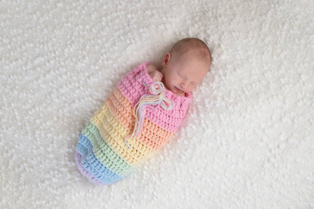 Newborn Baby Girl in a Rainbow Colored Pouch A three week old newborn baby girl bundled up in a rainbow colored snuggle sack. She is lying on a white, bouncle blanket. sack stock pictures, royalty-free photos & images