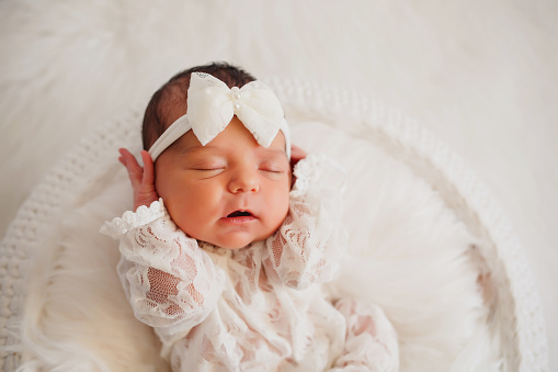Newborn baby girl sleeps in a white round basket covered with fur blanket; white background