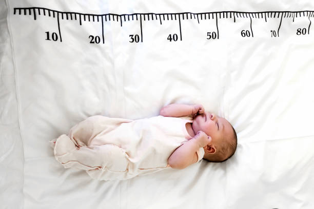 A newborn baby in white sleeps on a bed on which a measuring ruler for growth is drawn stock photo