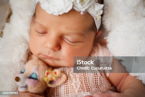 istock Newborn girl with a lion toy in her arms sleeps in the basket covered with white fur blanket on the floor 1310139192