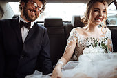 Newlyweds holding hands in the backseat