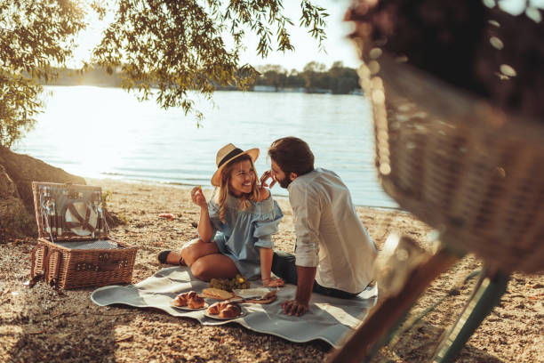 Next to you is the only place for me A young couple having a picnic at the beach picnic stock pictures, royalty-free photos & images