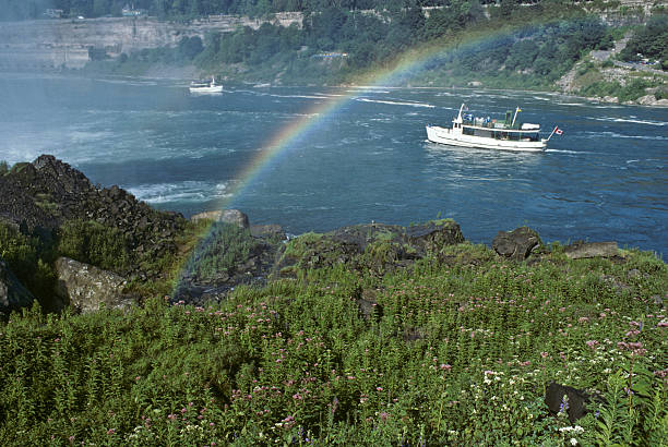 Maid of the Mist Under a Rainbow Niagara Falls is a great place to view and photograph rainbows. On any sunny day, rainbows are seen in the mist created by the falling water. The sun shines through the water droplets, reflecting light into the colors of the spectrum. Because the sun rises in the east, rainbows are seen in the morning from the United States side. Later in the day, as the sun gets higher, rainbows are seen on the Canadian side. This rainbow over the Maid of the Mist was photographed from the American Side at Niagara Falls, New York, USA. jeff goulden rainbow stock pictures, royalty-free photos & images